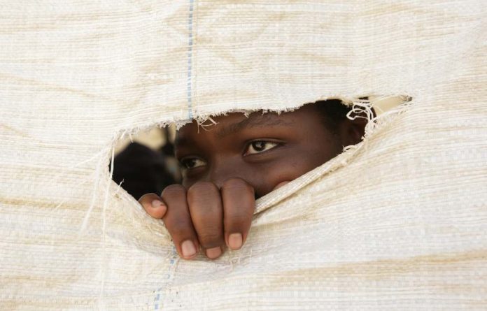 A Zimbabwean secondary school student peeps through a hole in a sack that forms the wall of a makeshift classroom.