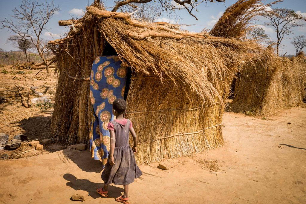 A girl beside her straw home, which offers little protection during the rains. (David Lee)